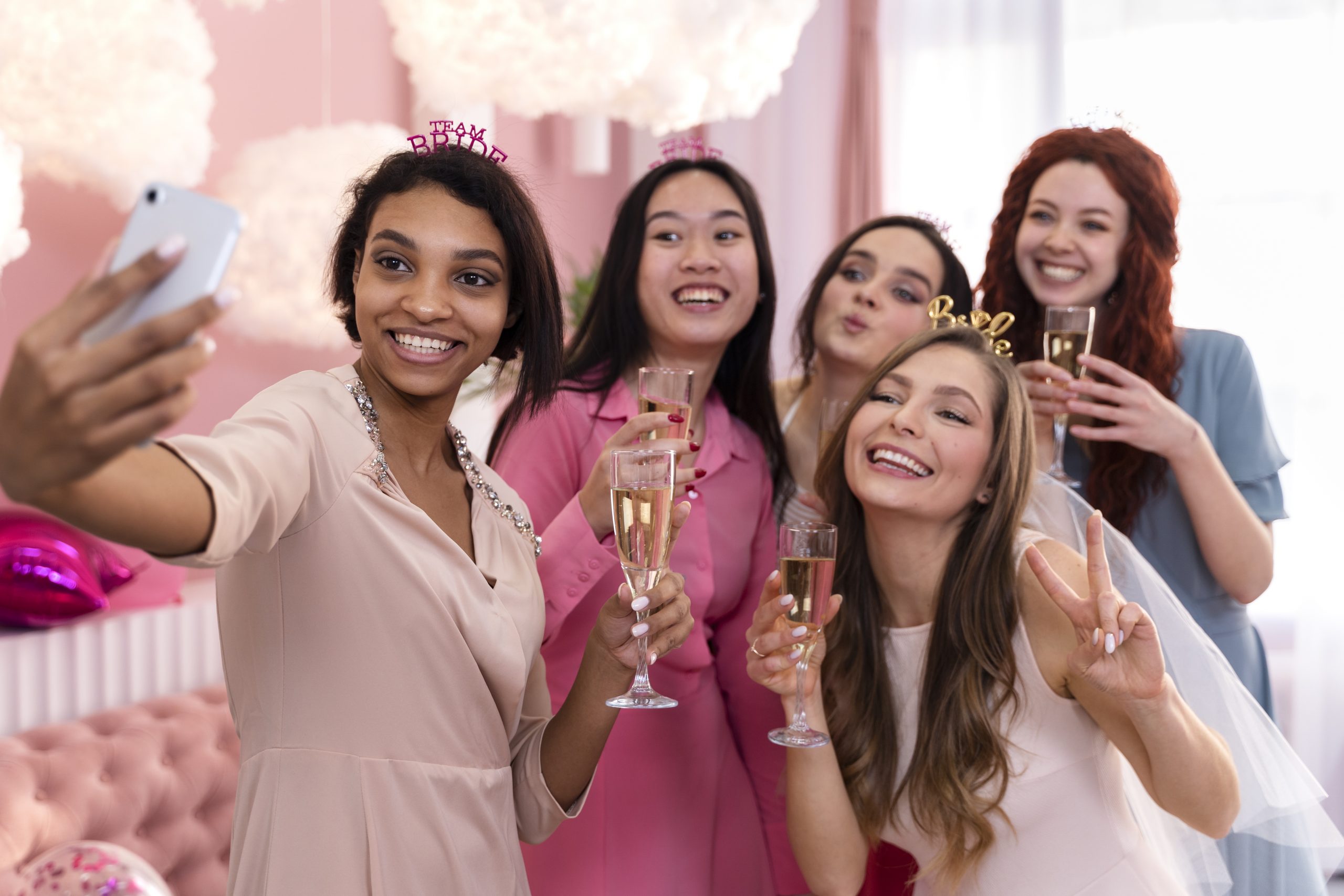 group of women pose for a selfie while toasting with champagne during a scavenger hunt app event. Girl on right is wearing a bride tiara.